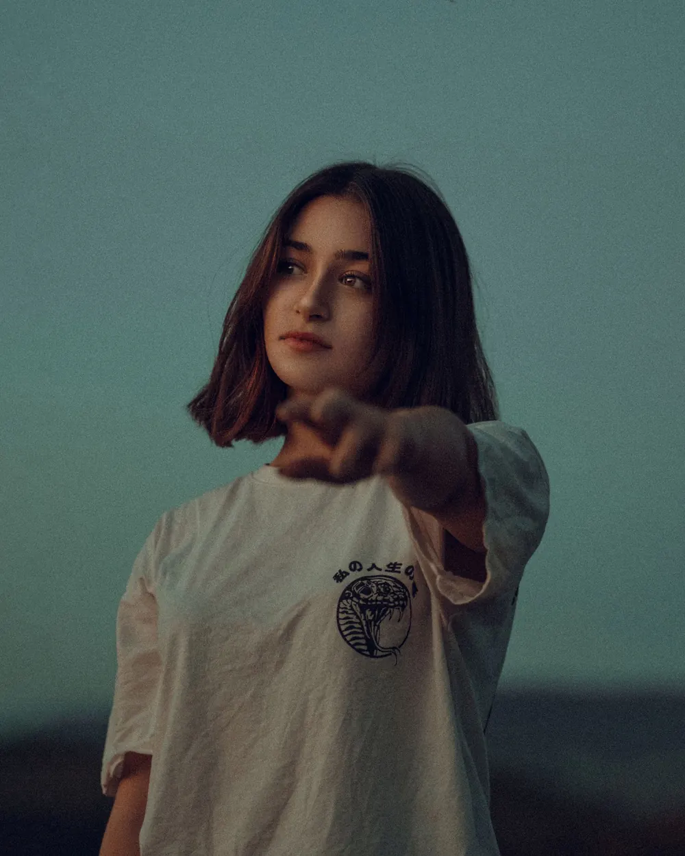 Artistic portrait of a young woman outdoors with her arm extended, capturing an introspective mood.