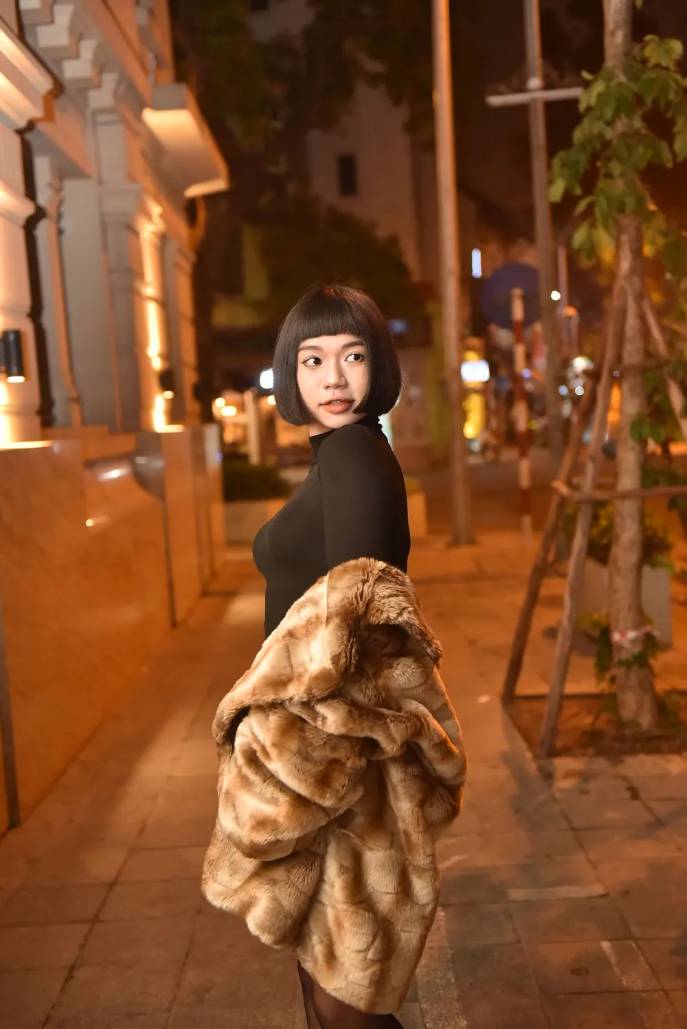 Chic portrait of a woman wearing a fur coat on a city street at night.