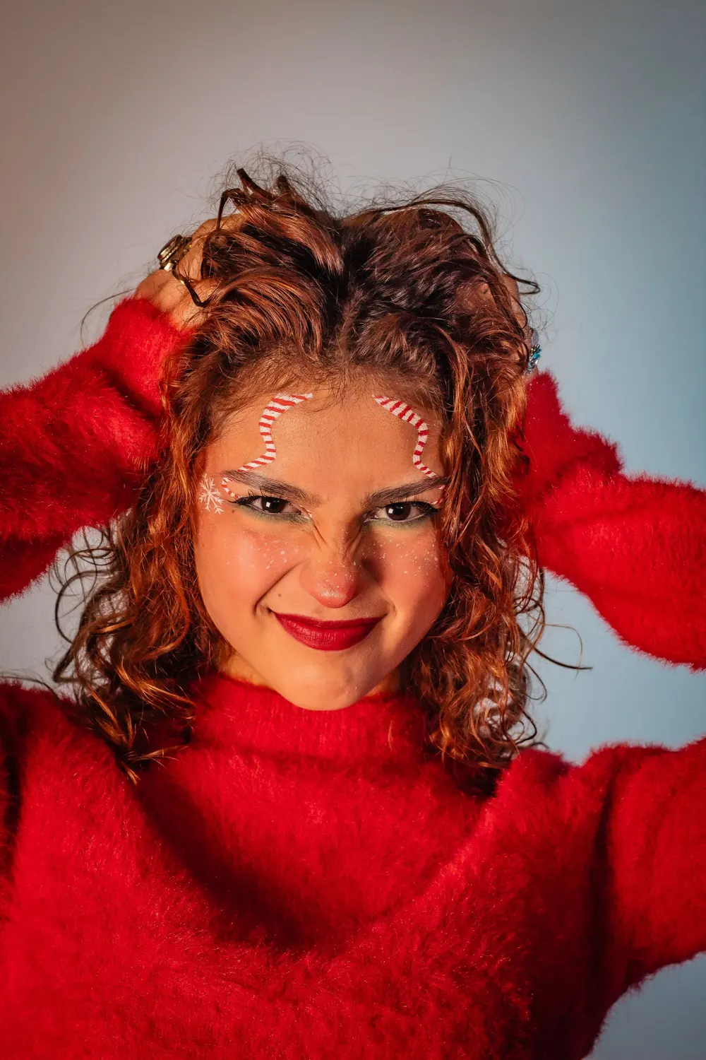 Young woman in a red sweater with festive makeup posing playfully indoors