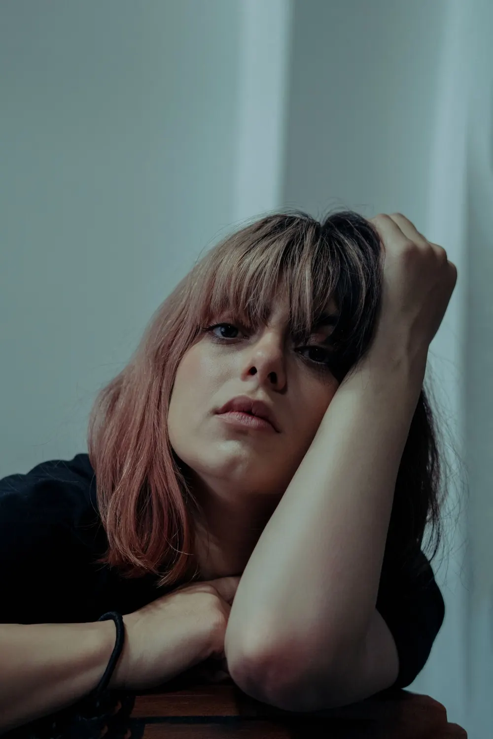 Close-up portrait of a young woman with pink dyed hair resting her arm thoughtfully.