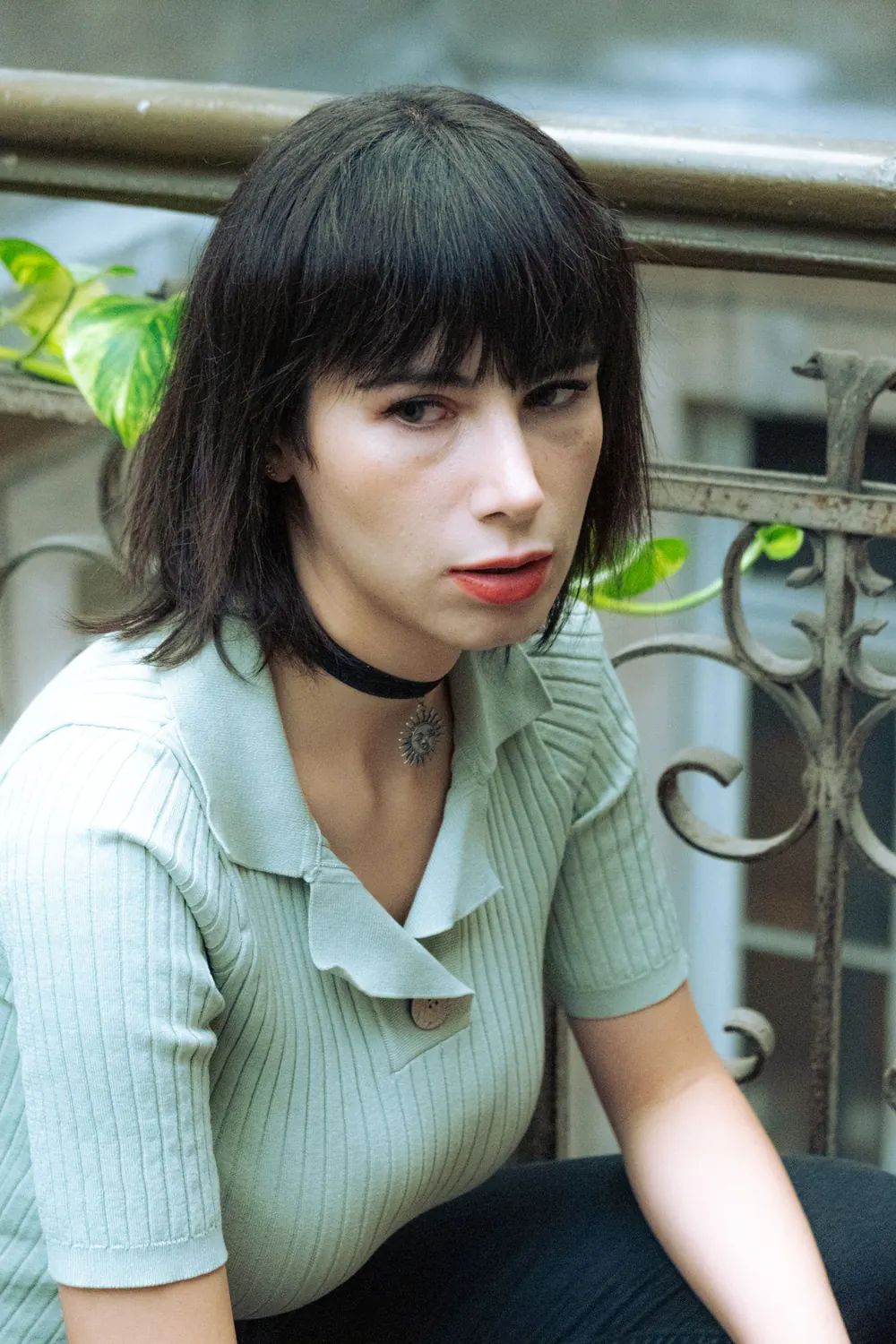 Close-up of a woman with short black hair and bangs sitting near metal railings.