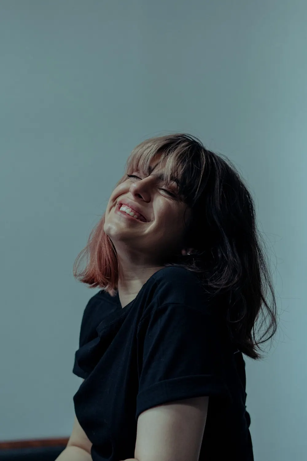 A cheerful woman with bangs smiling in an indoor setting, exuding happiness.