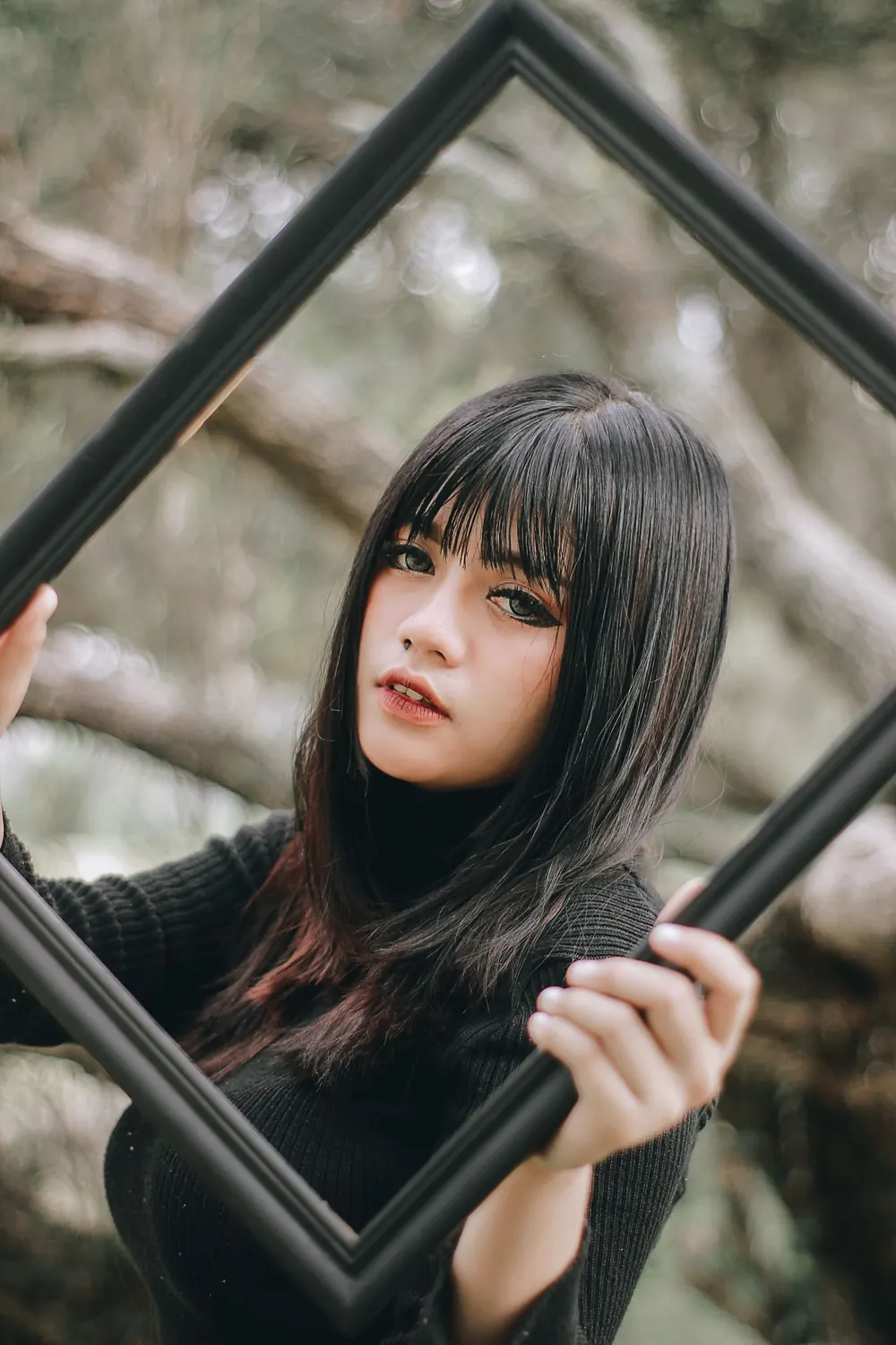 A fashionable portrait of a woman holding a black frame in a natural setting.