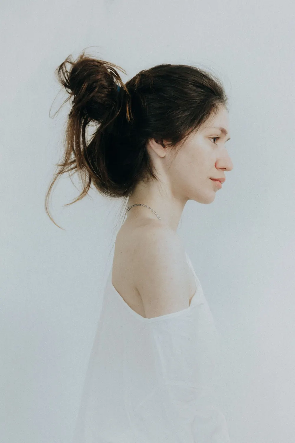 Elegant side profile portrait of a woman in a simple white top, showcasing minimalist beauty.
