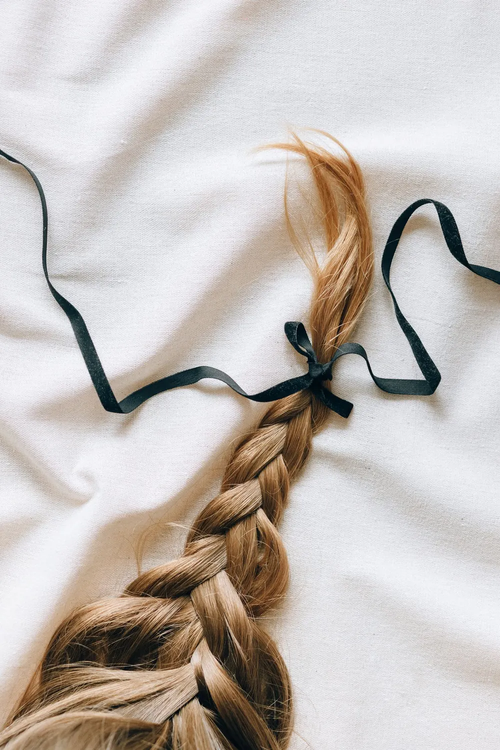 Close-up of a braided hairstyle adorned with a black ribbon on a white fabric background.