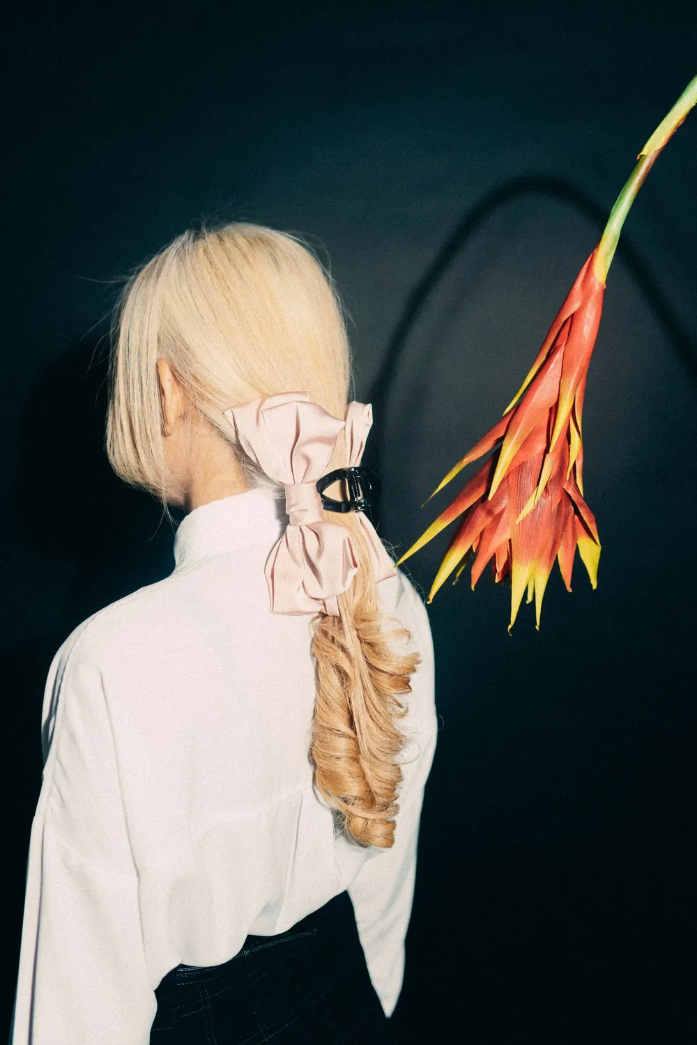 A stylish portrait of a woman with a floral accessory and fashionable hair styling against a dark backdrop.