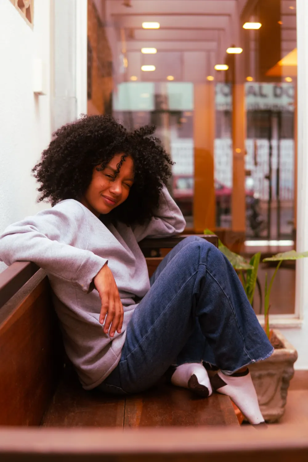 Woman relaxing casually on a bench indoors, exuding warmth and comfort.