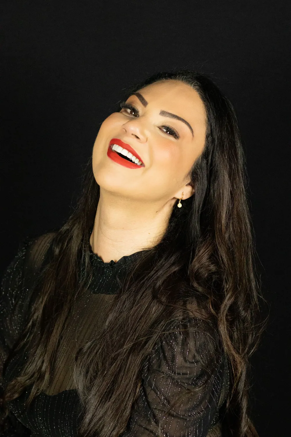 A glamorous studio portrait of a smiling woman with long hair and bright red lipstick.