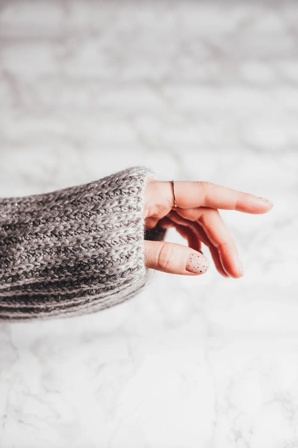 Close-up of a hand wearing jewelry and a cozy sweater on a marble background.